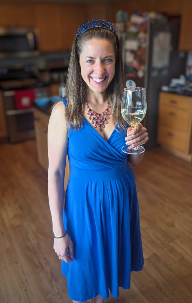 Laura standing in a blue dress with a white wine glass topped with red pop rocks